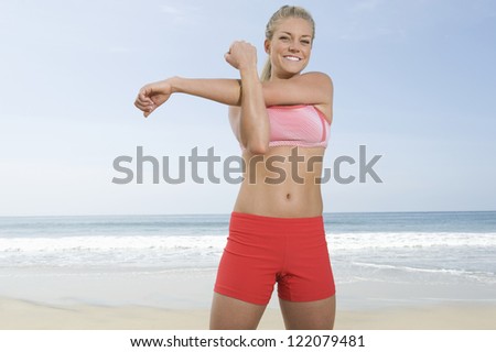 Portrait of healthy young woman doing arms exercises on beach