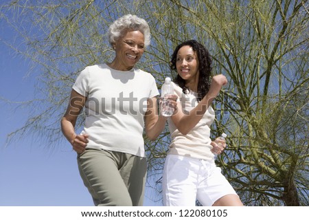 Happy African American mother and daughter jogging together against blue sky