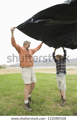 Full length of happy Caucasian father and son with tent holding tent cloth in garden