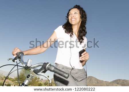 An African American  woman standing with a bicycle looking away while listening to music