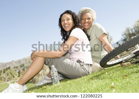 Portrait of happy African American mother and daughter sitting on grass