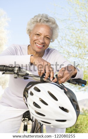 Portrait of a happy African American senior woman sitting on bicycle with helmet in hand