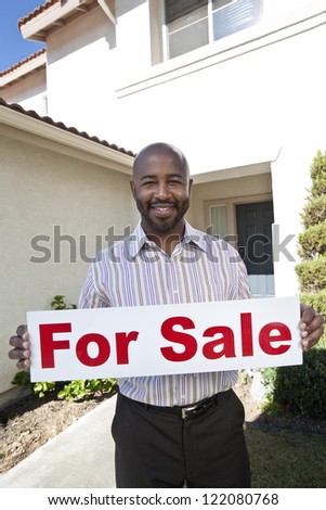 Portrait of a happy mature estate agent holding \'For Sale\' sign against house