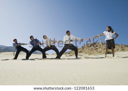 Full length of four multi ethnic businessmen playing tug of war against one woman in desert