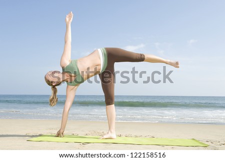 Full length of a woman in sportswear doing yoga (Half Moon pose) on mat at beach
