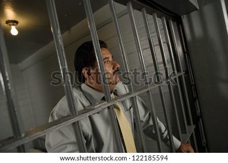 Sad businessman standing behind bars in prison