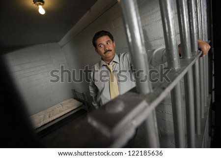 Sad businessman standing behind bars in prison