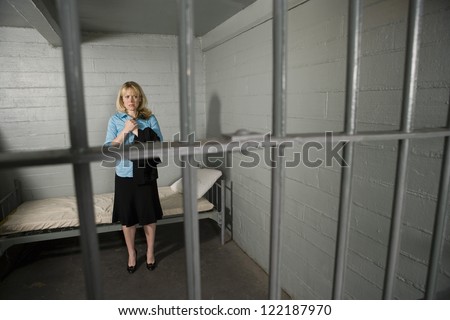Upset businesswoman standing behind bars in jail