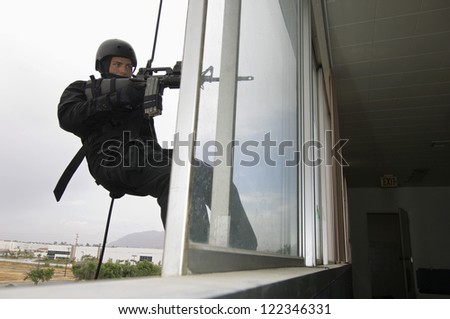 Armed man in military uniform hanging on the rope with gun outside window