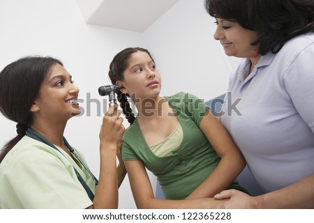 Doctor checking ear of teenage patient standing with mother