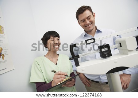 Happy man measuring weight with doctor making notes