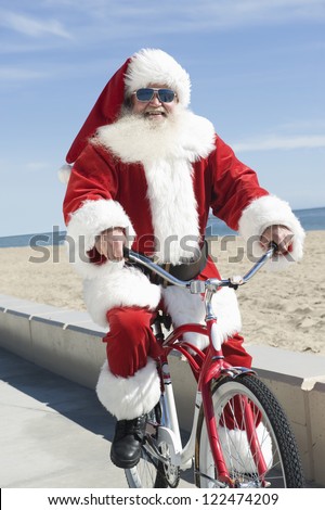 Portrait of happy Santa Claus riding cycle by the beach