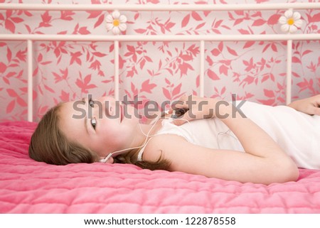Little girl listening music while lying on pink bed