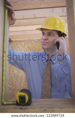 Young architect measuring wooden beam at construction site