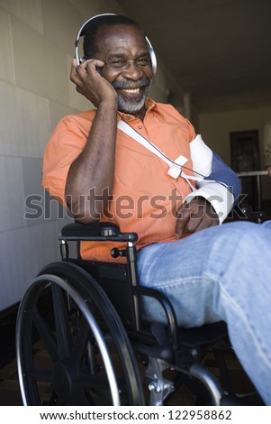 Injured senior African American man listening music on headphones while sitting in wheelchair