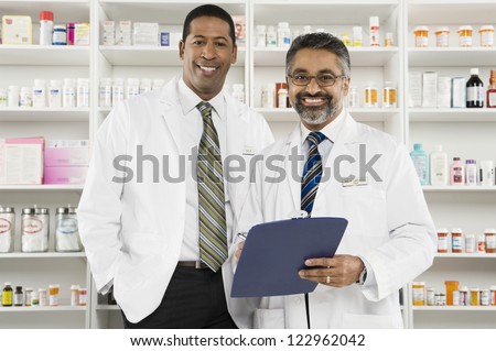 Portrait of a middle aged male pharmacist holding clipboard standing with coworker at workplace