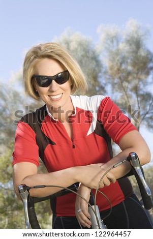 Portrait of a happy female cyclist leaning on bicycle