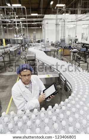High Angle View Of Man Examining Bottles At Bottling Plant