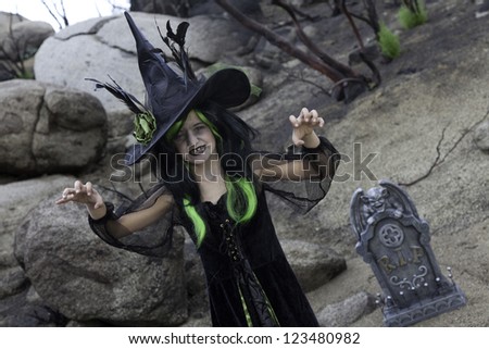 Girl in witch attire trying to scare you while standing in cemetery