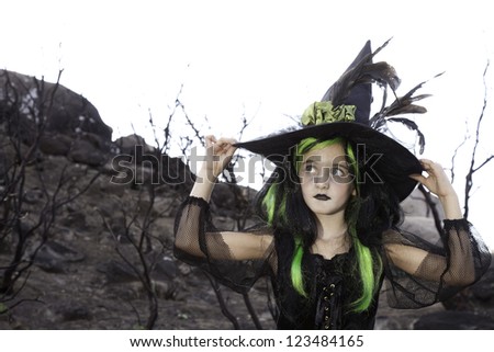 Pretty little witch holding her witch hat and looking away