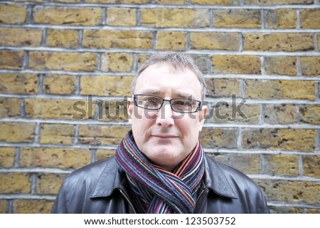 Portrait of a middle-aged man wearing glasses with scarf against wall