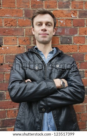 Portrait of man in leather jacket standing against brick wall