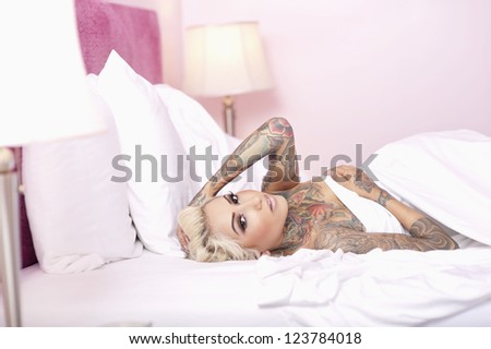 Portrait of a tattooed female lying on bed with hand in hair
