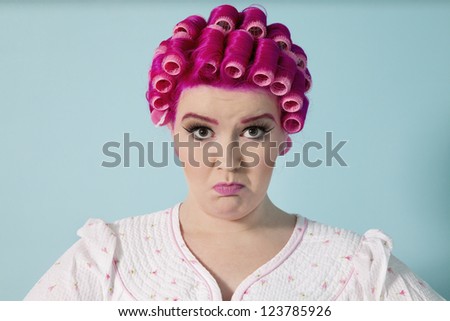 Portrait of young woman grimacing with hair curlers over colored background