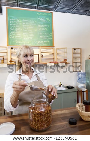 Happy senior female filling jar with scoop while looking away in store