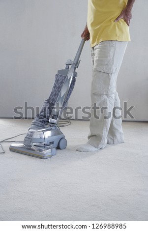Low section of man cleaning carpet with vacuum cleaner