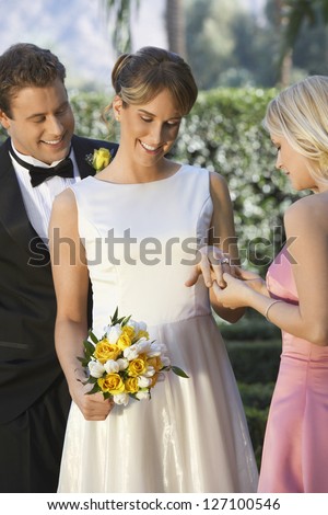 Beautiful bride showing her wedding ring to friend with husband standing in the background