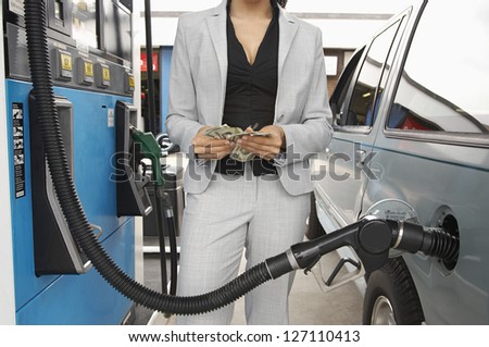 Mid section of a female counting money while waiting for refueling the tank of car