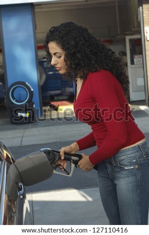 Side view of beautiful woman inserting nozzle in a car tank