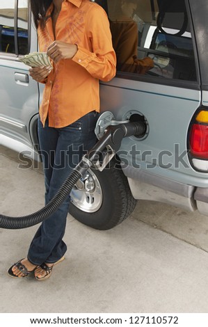 Low section of female counting money while leaning on car at petrol pump