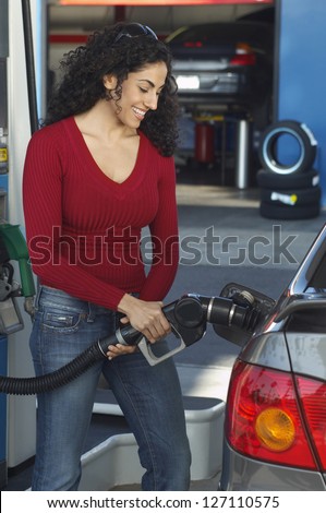 Happy woman refueling car tank at petrol station