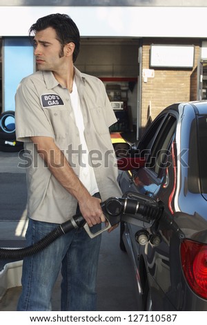 Gas station worker refueling the car tank while looking over shoulder at petrol station