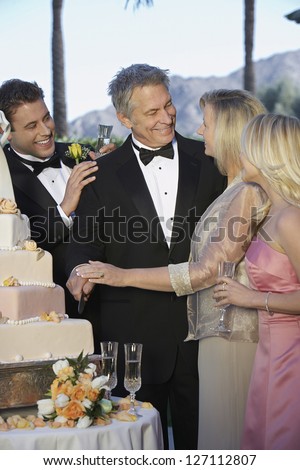 Happy couple with young man and woman gathered near wedding cake