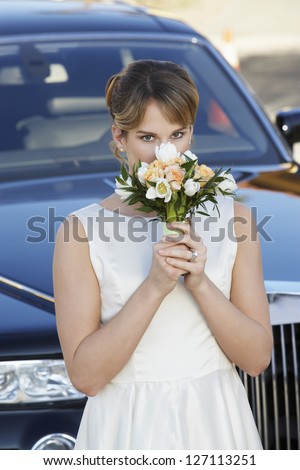Portrait of beautiful woman smelling the fragrance of rose with car in the background