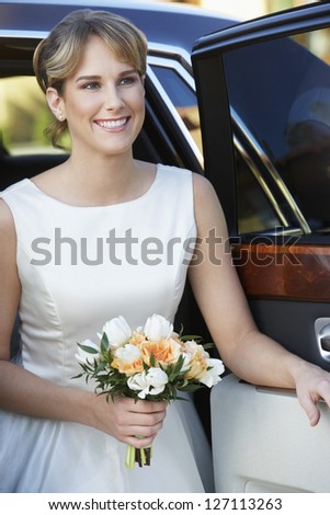Beautiful bride getting down from car while holding roses