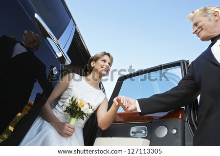 Low angle view of beautiful bride getting down from car while holding father\'s hand