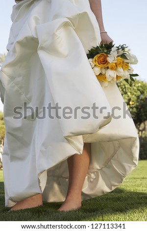 Low section of a bride in a wedding dress holding bunch of roses at lawn