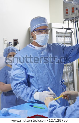 Male surgeon making preparing before surgery with nurse assisting him in operating room