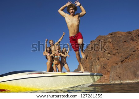 Low angle view of man jumping in water with friends standing in the background (Soft focus)