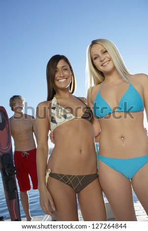 Low angle view of a happy young female friends in bikini standing together with man standing in the background
