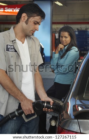 Petrol pump worker removing nozzle from fuel tank of a car with woman in the background