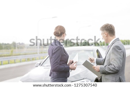 Insurance agent discussing with businesswoman while pointing at breakdown car against sky