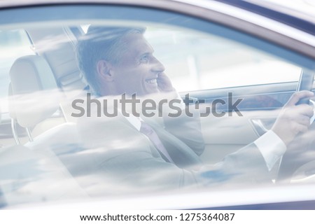 Smiling mature businessman talking on mobile phone while driving car