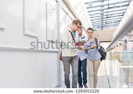 Students exchanging books while walking in corridor at college