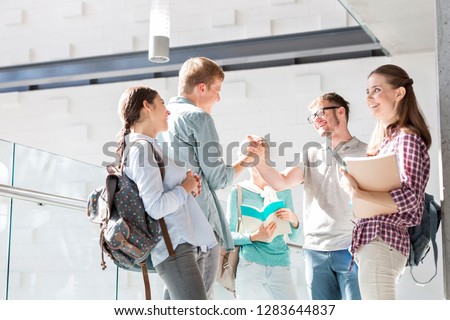 Happy friends greeting while standing in university corridor
