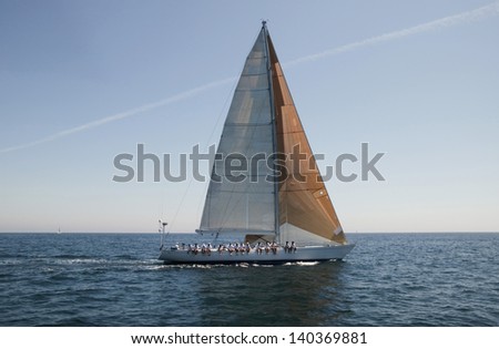 Side view of a group of crew members sitting on the side of a sailboat in the ocean against sky